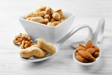 Pistachios, almonds, peanuts and walnut kernels in the ceramic bowl and spoons, on white wooden background