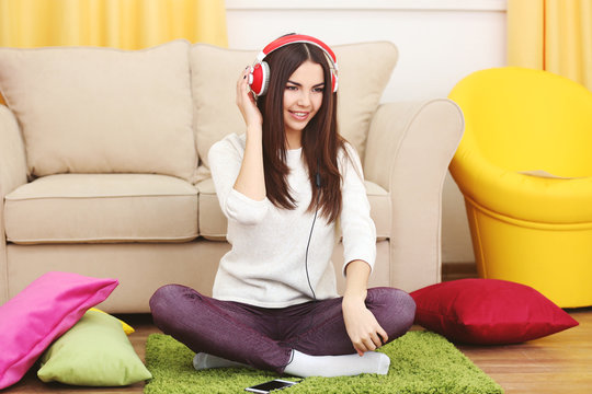 Happy young woman with headphones listening to music on a floor at home