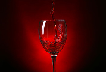 Wine pouring in glass on dark red background