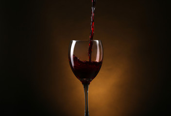 Wine pouring in glass on brown background