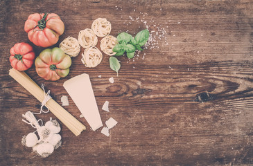 Ingredients for cooking pasta. Spaghetti, tagliatelle, garlic, Parmesan cheese, tomatoes and fresh basil on rustic wooden background, top view, copy space.