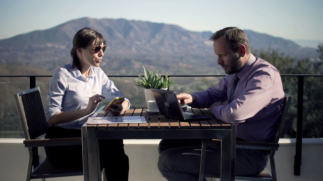 Young business couple working with smartphone and laptop by table at home 
