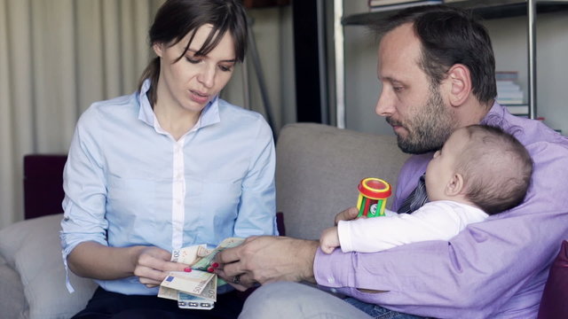 Young sad couple with child counting money sitting on sofa at home
