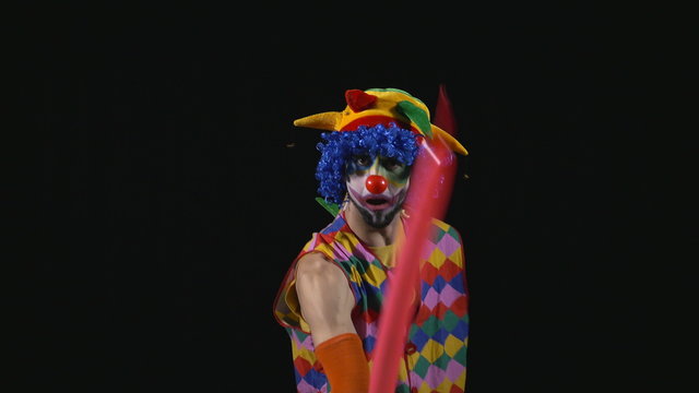 Young funny clown making a dog from a balloon and bursting it with a needle