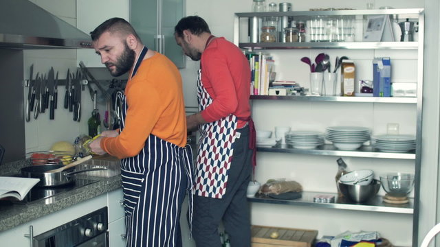 Two men in aprons cooking in the kitchen at home
