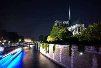 Fototapeta na wymiar Bateau Bleu - Long exposure night photo of Notre Dame cathedral and the Seine River with the blur of a passing tour boat.