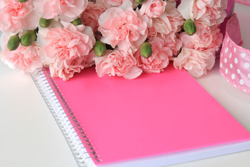 A pink notebook and bouquet of flowers with a ribbon on a white desktop background.