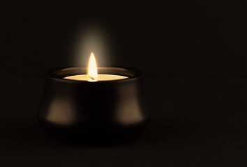 Candle in small holder glowing brightly in the dark