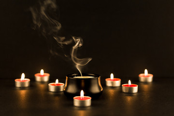 Group of burning candles and a big candle extinguished in the middle with intricate smoke patter...