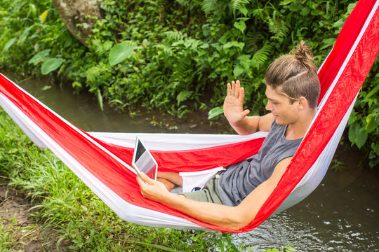 Man in hammock working on laptop during summer holidays.