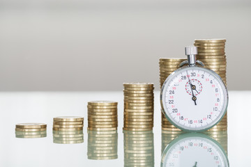 Stopwatch And Stacked Coins On Desk