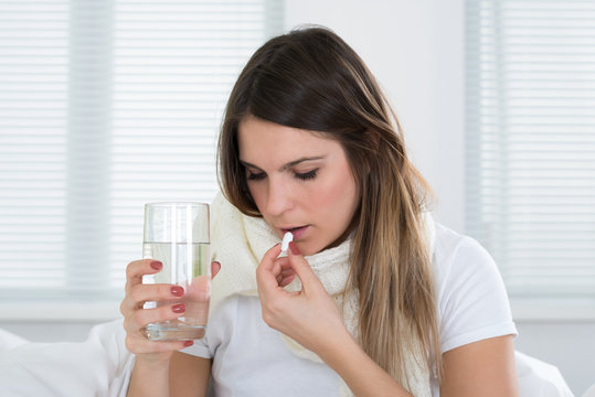 Young Woman Taking Pills And Glass Of Water