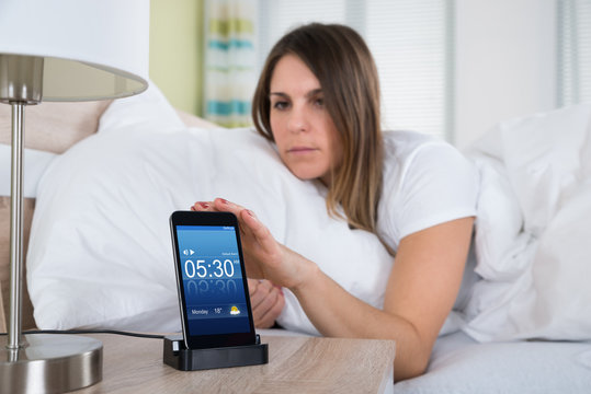 Woman On Bed Snoozing Alarm On Mobile Phone