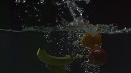Close up of fresh ripe fruits falling into water and floating in it against black background  - Powered by Adobe
