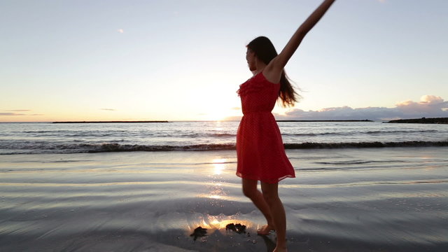 Beach woman having fun spinning around dancing at sunset enjoying freedom during summer holidays vacation travel. Beautiful happy young mixed race Asian Caucasian female model outside.
