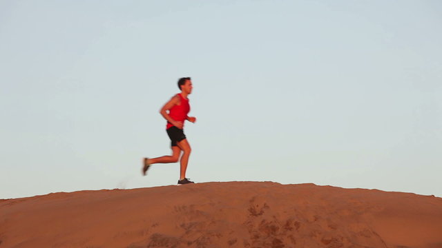 Running man in desert. Male athlete runner training for ultra marathon jogging dune in desert. Fit sports fitness model in amazing extreme desert landscape nature at sunset with jogging male athlete.