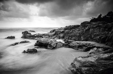 black and white image of wave hitting the rock. dark and dramatic clouds. soft focus due to long...