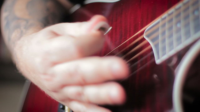 Man with Tatoo playing acoustic guitar