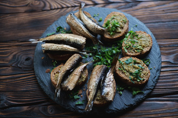 Stone slate with smoked sprats sandwiches, selective focus