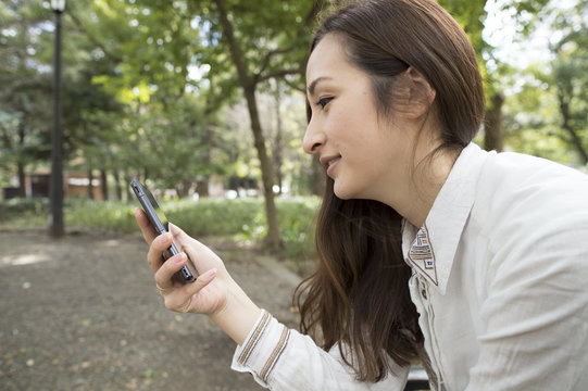 Women are using a smart phone sitting on a bench in the park