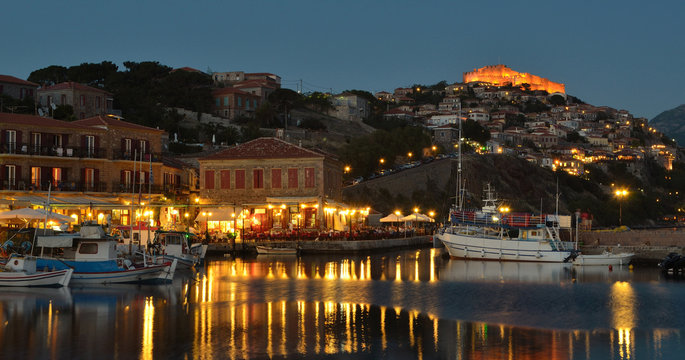 People eating in harbor side restaurants in the early evening, castle and quayside illuminated.
