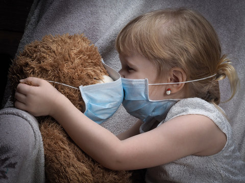 Kiss through the medical mask. A small child kisses teddy bear. Toy and children in masks.