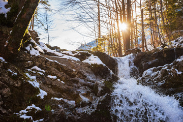 Gebirgsbach mit Wasserfall im Winter, strahlender Sonnenschein