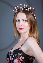 Fototapeta premium studio portrait of young beautiful sexy woman with wreath made of red and white artificial berries, stylish makeup and red lips on gray background