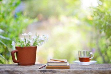 tea in glass and notebook with flower pot on wooden table at outside