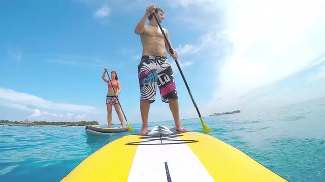 Happy young couple SUP boarding on beautiful blue ocean in Maldives