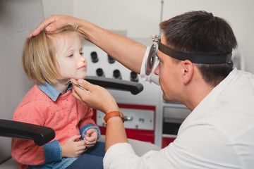 Doctor ENT checking ear with otoscope to girl patient 