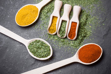 Three wooden spoons with colorful spices on black background.