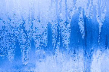 Bright blue thawing frost pattern on a window glass