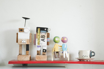 Colorful mini wooden robot models and coffee cup on red shelf