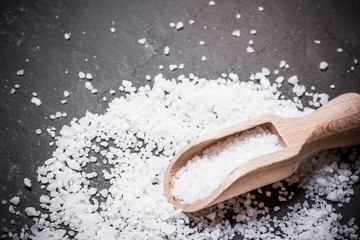 White sea salt on wooden spoon on black surface.