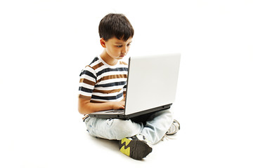 Young schoolboy is sitting on floor and surfing on his laptop. Isolated on white background 