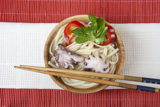 Noodles with octopus anp papper in wooden plate on a red makisu