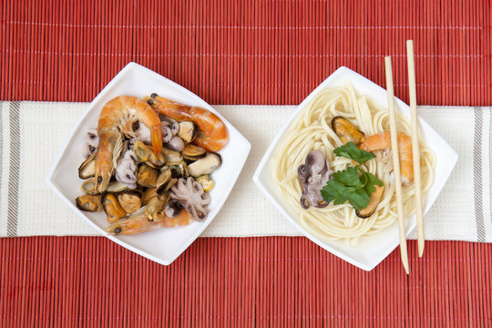 Noodles with shrimp, mussels and octopus in white plate on a red makisu