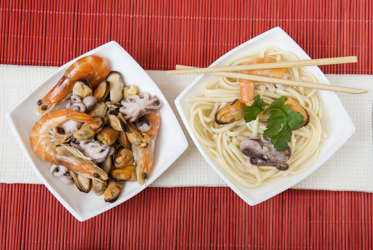 Noodles with shrimp, mussels and octopus in white plate on a red makisu