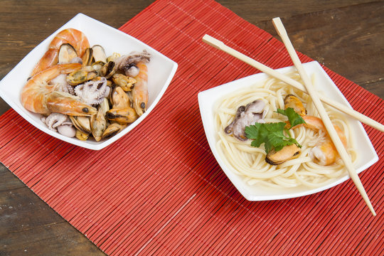 Noodles with shrimp, mussels and octopus in white plate on a red makisu