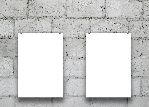 Close-up of two hanged paper sheets with clothes hangers on grey concrete block wall background