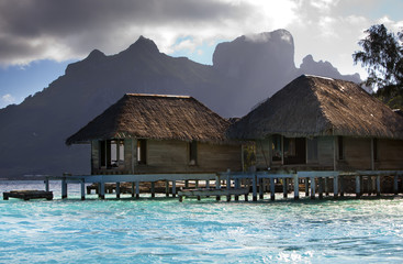 the destroyed thrown huts on water  in the ocean and mountains on a background