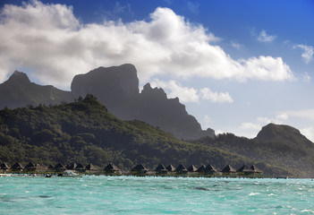 Obraz premium island with palm trees and small houses on water in the ocean and mountains on a background