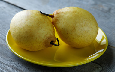 Two yellow pears on the plate on a rustic table