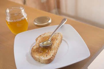 Tostada con miel en un plato blanco con luz natural encima de una mesa. Desayuno.