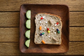 Various drugs and pills on a slice of granary bread on a wooden plate at a table setting