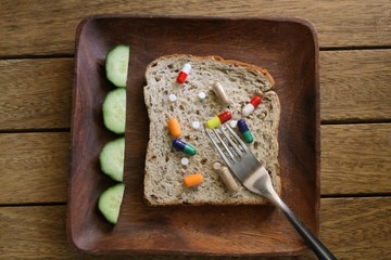 Various drugs and pills on a slice of granary bread on a wooden plate at a table setting