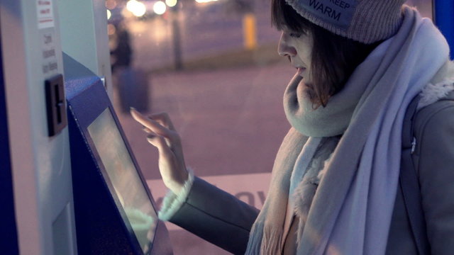 Young woman buying ticket from vending machine at tram station
