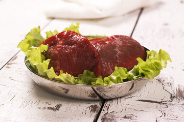 Raw meat with lettuce over white wooden table. Selective focus