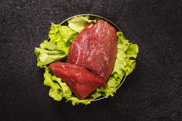 Raw meat with lettuce over black stone background. Top view. Selective focus